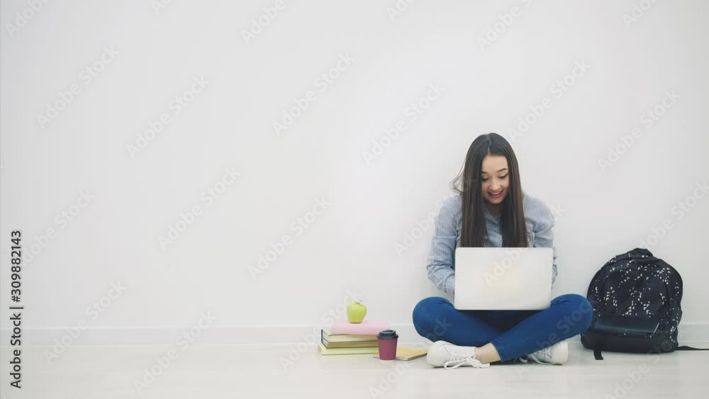 Asian lady sitting on the floor in lotos position, with laptop, raising up her hands, waving them and smiling happily as a winner. Asian lady sitting on the floor in lotos position, with laptop, raising up her hands, waving them and smiling happily as a winner.