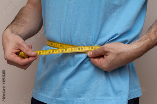 man in a blue T-shirt measures the waist with a yellow tape photo