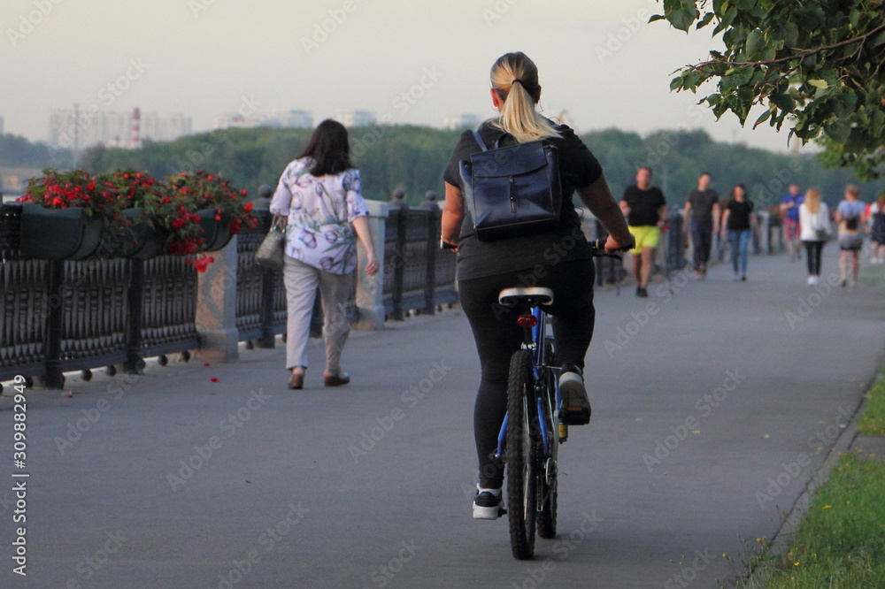 A woman with long hair on a Bicycle ride on an asphalt road in the Park on a summer Sunny evening, active urban recreation