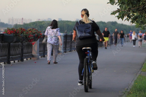 A woman with long hair on a Bicycle ride on an asphalt road in the Park on a summer Sunny evening, active urban recreation © Ilya
