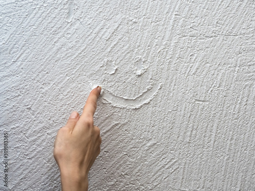 Finger paints a smiley face on a white stucco wall.