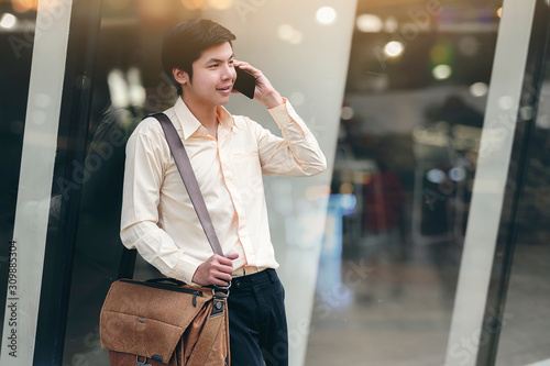 Portrait of handsone businessman with sling bag using mobile outdoors. photo