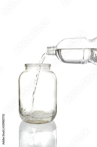 Pouring water into an empty glass jar on a white background