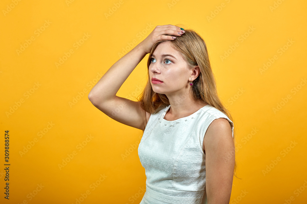 Disappointed caucasian young lady keeping hand on head, heaache, looking aside over isolated orange background wearing white shirt. Lifestyle concept