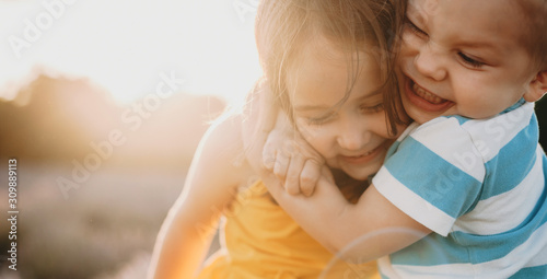 Close up portrait of a lovely little kid embracing with love his sister against sunset. photo