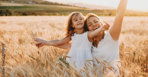 Portrait of a happy young mother and her lovely daughter playing and laughing in a field of wheat . Freedom concept. photo