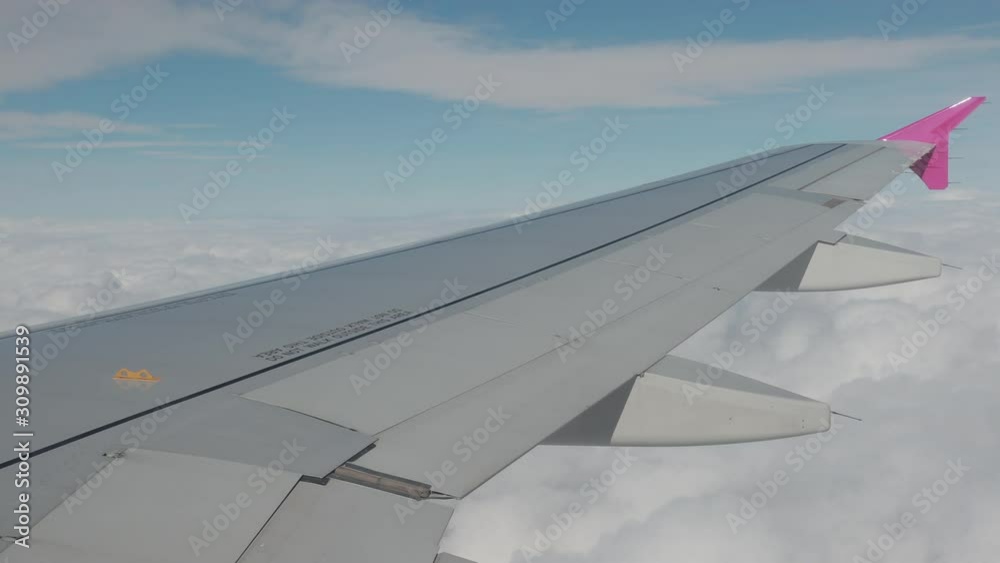 Amazing view on plane wing of grey, pink colours. Behind airplane there are lots of white fluffy clouds, bright day blue sky. Amazing view on plane wing of grey, pink colours. Behind airplane there are lots of white fluffy clouds, bright day blue sky.