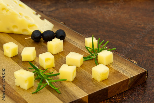 sliced cheese with olives and rosemary on a wooden board. wine cheese appetizer