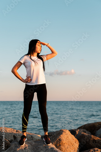 The concept of sport and a healthy lifestyle. A young woman in sports clothes , standing on the coastal rocks, resting her hand on hips and looking into the distance. Copy space