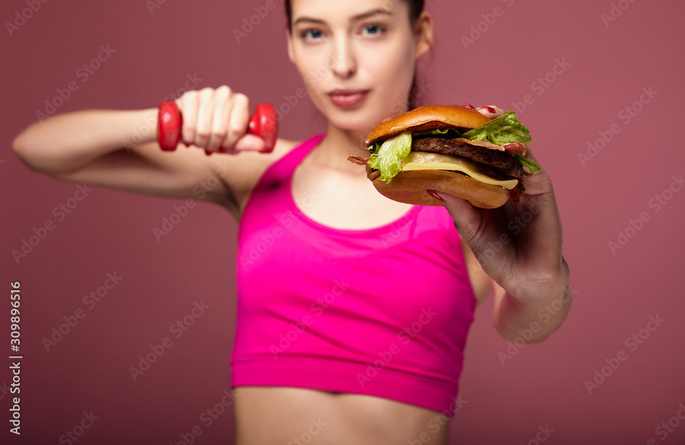 Girl with a burger posing in the gym. Girl with a burger posing in the gym.