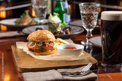 Bild auf Leinwand Delicious burger and glass of dark beer on wooden table at restaurant