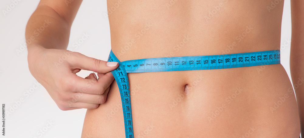 Close up slim young woman measuring her thin waist with a tape measure.  Stock Photo