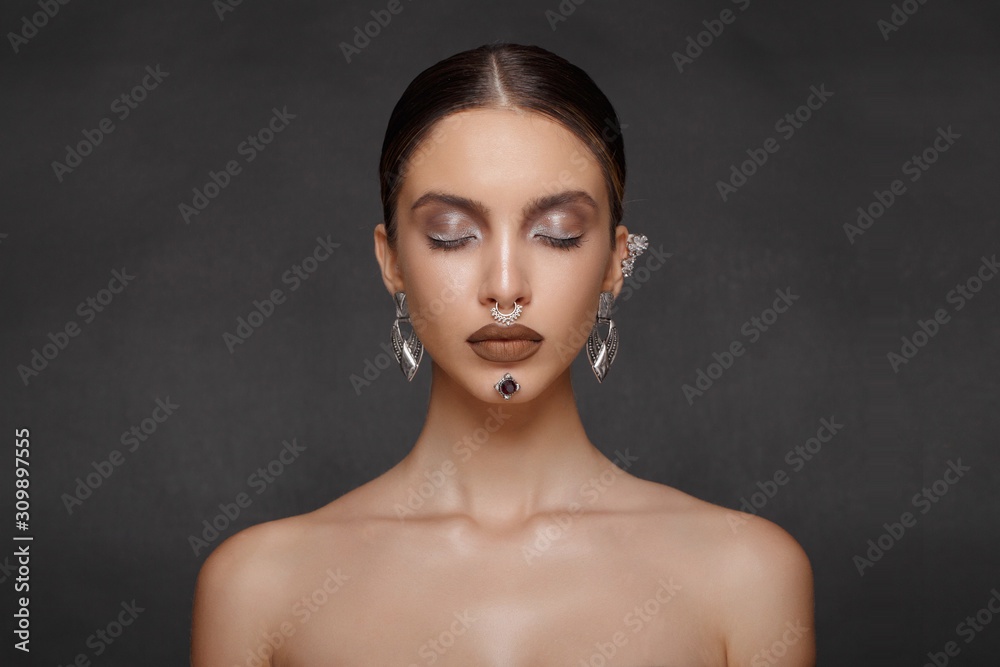 Beautiful girl with a jewelry on grey background, eyes closed. Frontal beauty portrait. Makeup, cosmetics, hairstyle, bijouterie. Beautiful girl with a jewelry on grey background, eyes closed. Frontal beauty portrait. Makeup, cosmetics, hairstyle, bijouterie.