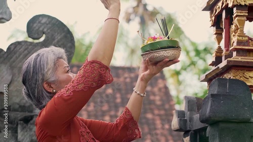 beautiful and happy Asian Indonesian woman dressed in traditional Balinese religious custom holding incense stick and flowers offering outdoors at Bali temple photo