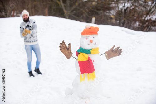 Have fun winter day. Let it snow. Christmas holidays. Active lifestyle. Snow games. Leisure on fresh air. Snowman and cheerful bearded hipster knitted hat and warm gloves play with snow outdoors