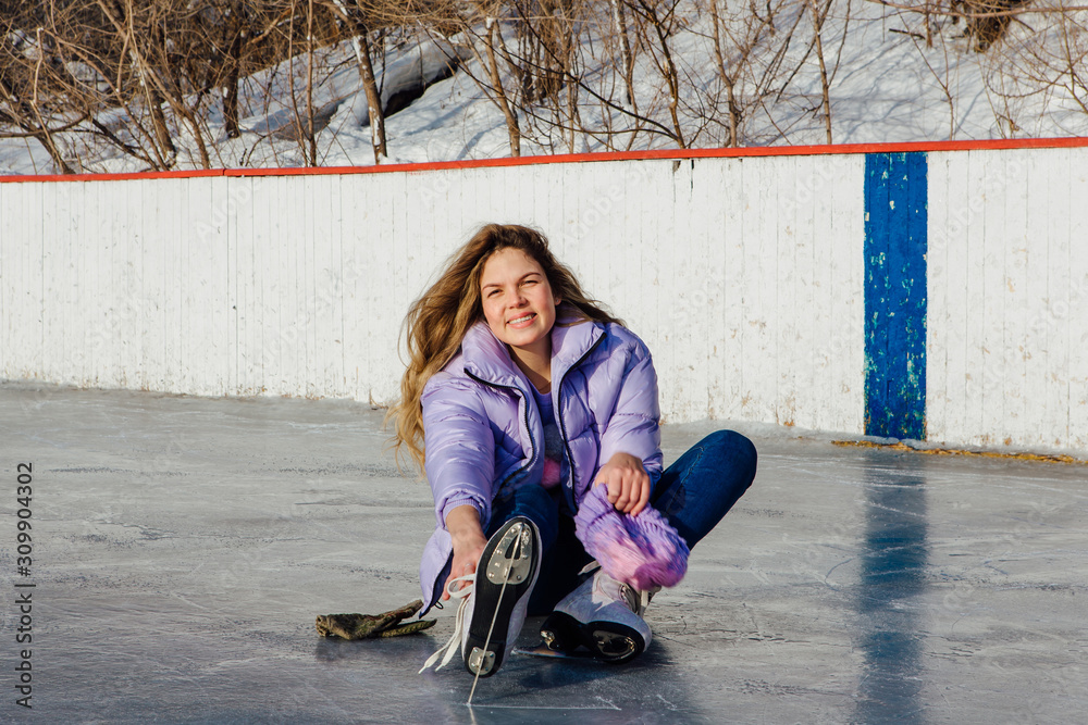 Lovely young woman sitting on ice ring and tieing shoelaces Lovely young woman sitting on ice ring and tieing shoelaces