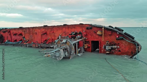 cargo ship lies on its side, near the shore of a sandy beach with a barrier to the pollution zone after the ship wreck. aerial drone shot.