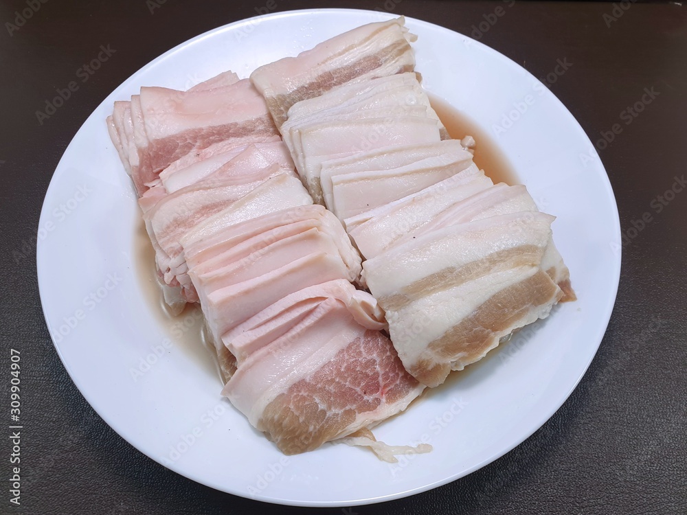 Raw meat, Top view of pork belly on white plate isolated on wooden background in restaurant, fresh meat for grill or cooking, Kurobuta Bara is japanese traditional