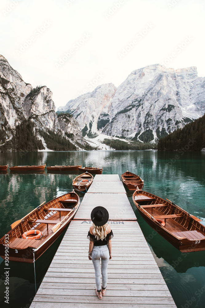 Young adventurer-traveler female standing on a wooden pier at the famous place in the Dolomities,Lago Di Braies lake,Italy,Europe.