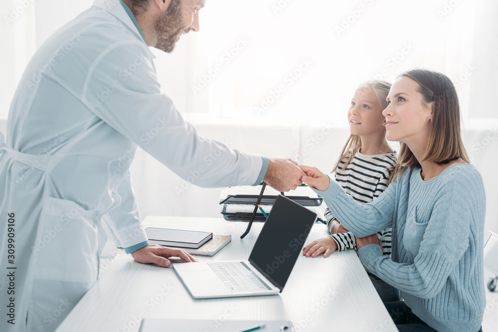 Fototapeta premium positive doctor shaking hands with mother of cute child