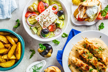 Greek food: greek salad, chicken souvlaki, gyros and baked potato wedges on gray background, top view. Traditional greek cuisine concept.