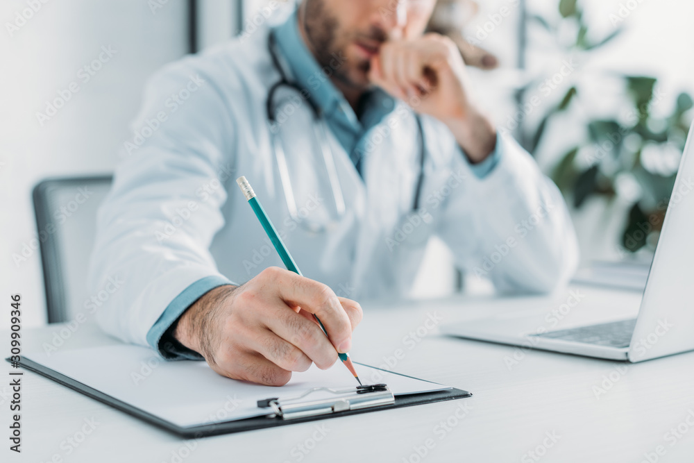 partial view of doctor writing prescription on clipboard partial view of doctor writing prescription on clipboard
