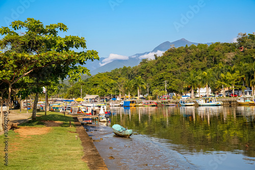 Idyllic view of river Perequê-Açu at lowe tide with colorful tour boats, trees and rainforest mountains on a sunny day in Unesco World Heritage town Paraty, Brazil