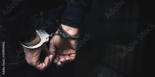 Fotografiet handcuffed arrested man behind prison bars. copy space