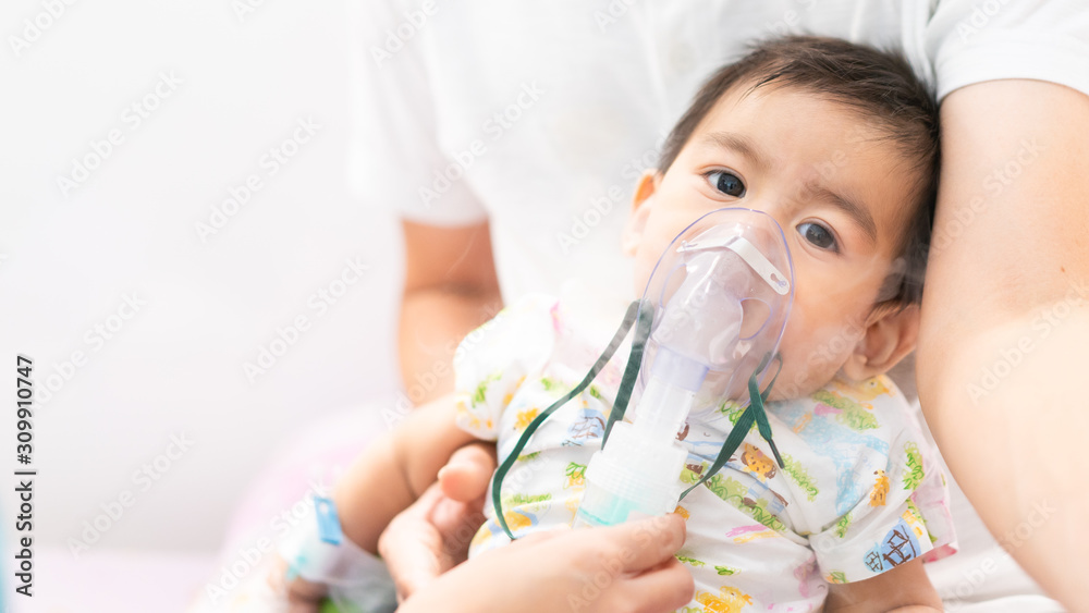 Close up of asian little baby boy is treated respiratory problem with vapor nebulizer to relief cough symptom in the hospital room , concept of pediatric patient care for sick in the hospital. Close up of asian little baby boy is treated respiratory problem with vapor nebulizer to relief cough symptom in the hospital room , concept of pediatric patient care for sick in the hospital.