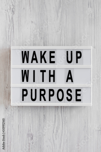 'Wake up with a purpose' words on a lightbox on a white wooden background, top view. Overhead, from above, flat lay. Close-up.