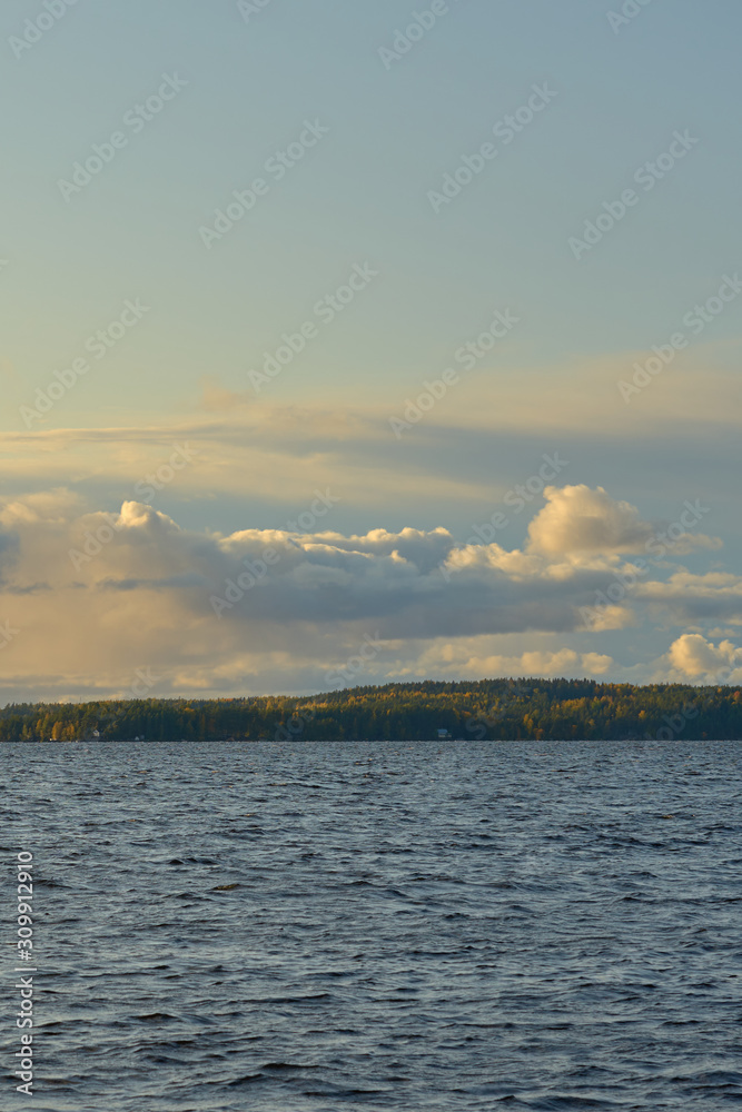 Rocks in the midle of a lake with cloudy sky and autumn forest on a background. Copy space.