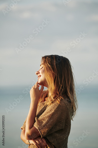Happy attractive young woman standing in sunset sun rays when spending time on the beach