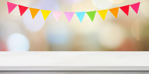 Colorful bunting party flags hanging onblur abstract bokeh light and white marble table background, birthday, anniversary, celebrate event, festival greeting card background, banner, backgdrop