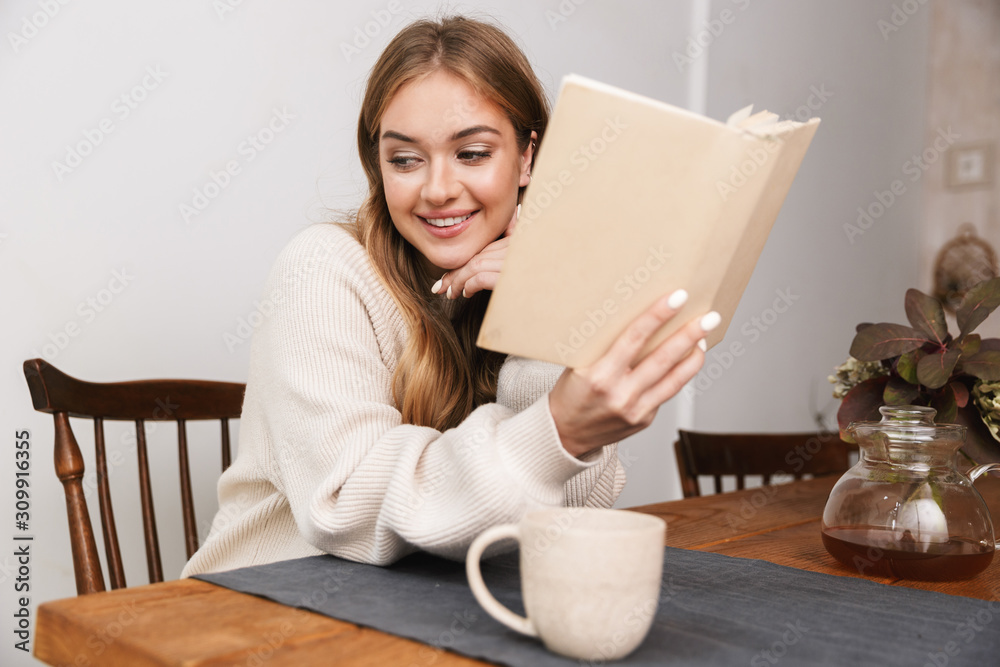 Image of smiling caucasian woman reading book and drinking tea Image of smiling caucasian woman reading book and drinking tea