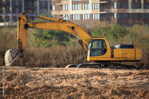 Excavator (digger) with a huge bucket at a construction site. Construction machinery at the facility. Building a new housing estate. Construction of modern multi-storey walled residential buildings
