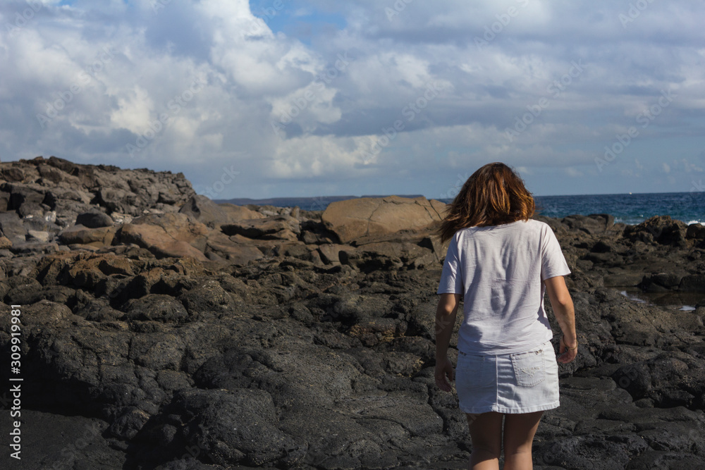 Women with summer clothes on volcanic rocks and blue ocean
