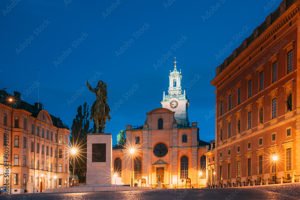 Stockholm, Sweden. Statue Of Swedish King Karl XIV Johan Sitting On A Horse Near Great Church Or Church Of St. Nicholas And Royal Palace. Famous Popular Destination Scenic Place In Night Lights