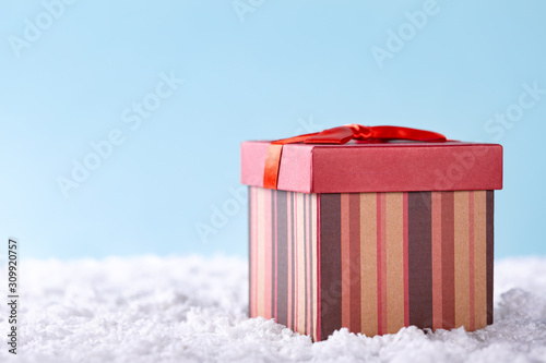 Christmas red gift box on snow over blue background. Winter holidays