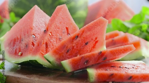 Sliced juicy watermelon on a wooden board. Composition of ripe watermelon and fresh mint on the kitchen table. Ripe summer watermelon. Concept of seasonal fruits on the table G