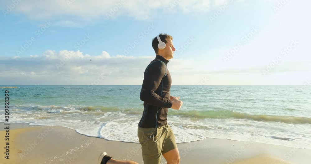 Fit male runner training on the summer beach and listen to music against beautidul sky and sea , UHD 4K