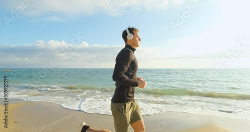 Fit male runner training on the summer beach and listen to music against beautidul sky and sea , UHD 4K