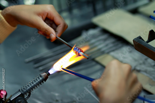 Artist of glass at work. Hand made glass beads in the fire out of red hot glowing glass for pandora bracelets,focus glass bead around blurry