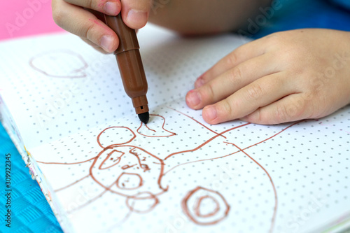 girl draws with felt-tip pens on a colored background. brown drawing on a white sheet. children's creativity