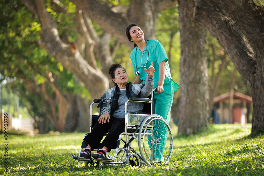 Asian senior woman sitting on the wheelchair with woman in doctor uniform in the park hospital Asian senior woman sitting on the wheelchair with woman in doctor uniform in the park hospital