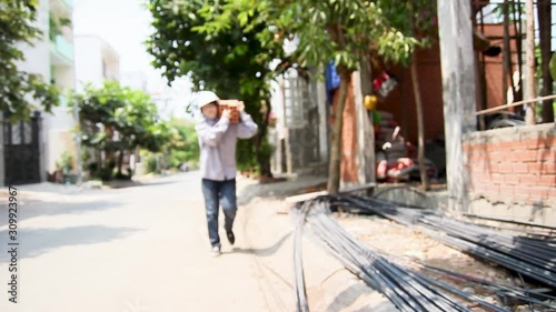 Blue collar worker bringing brick under sunlight in construction building zone in Vietnam. A young women working in harsh environment