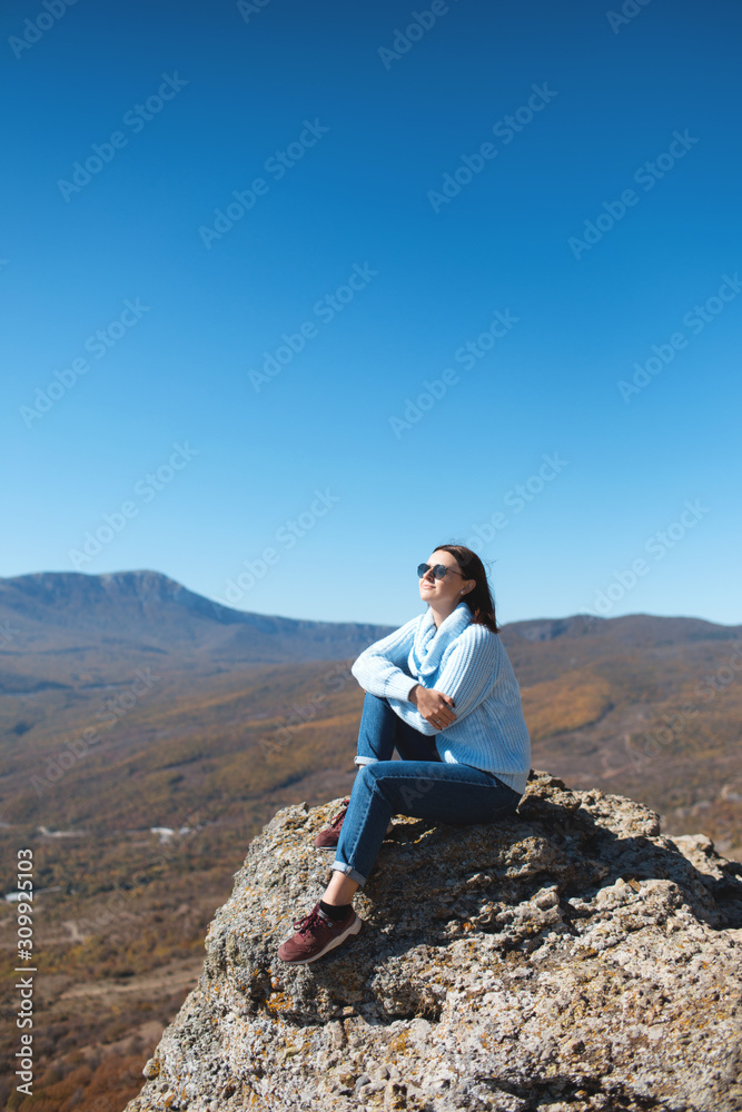 A girl sits on a rock in the mountains and enjoying view of nature. Nature background. Journey. A trip to the mountains. A girl sits on a rock in the mountains and enjoying view of nature. Nature background. Journey. A trip to the mountains.