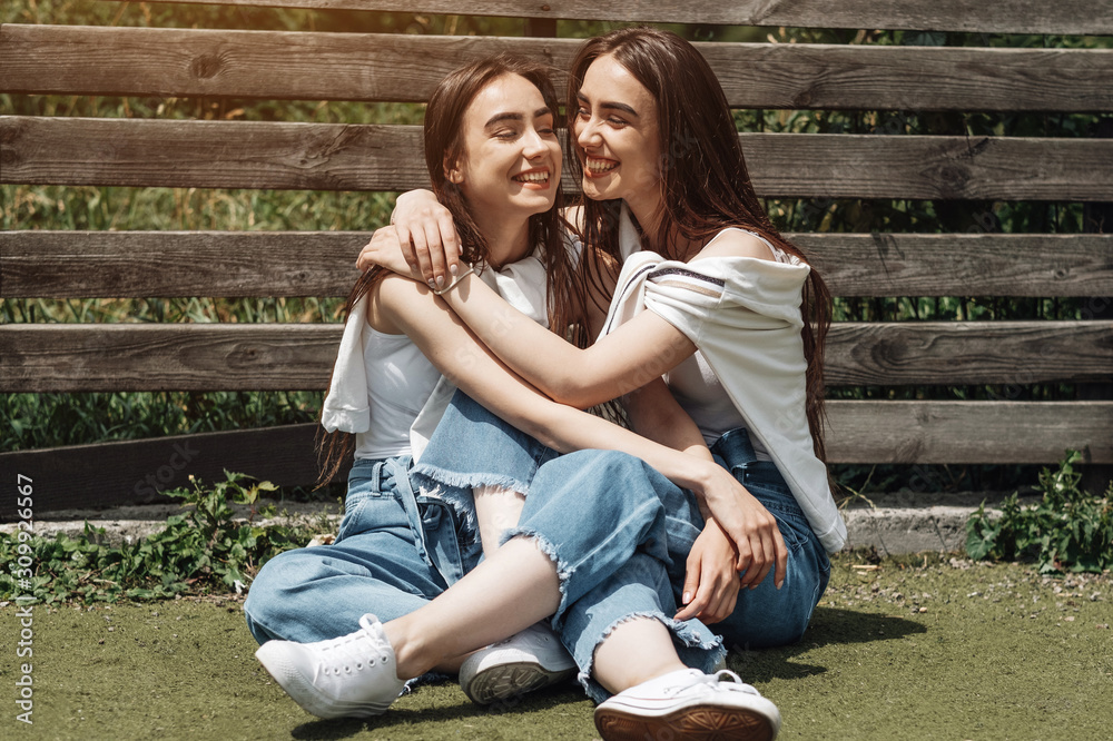 Portrait of Two Young Brunette Twins Sisters Dressed Alike in Jeans and White T-shirt, Best Friends Forever Concept Portrait of Two Young Brunette Twins Sisters Dressed Alike in Jeans and White T-shirt, Best Friends Forever Concept