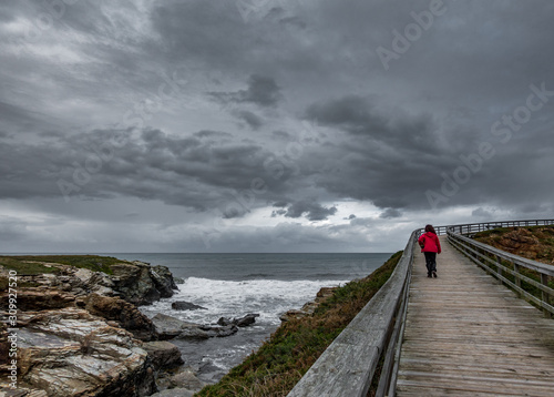 Wooden track through the ocean with hiker under gray sky