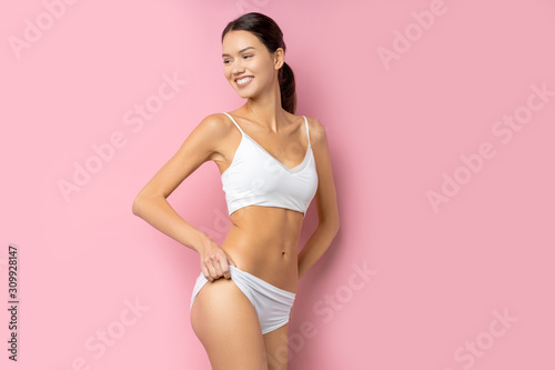 portrait of beautiful woman with slim sportive athletic body isolated over pink background, wearing white underwear or lingerie
