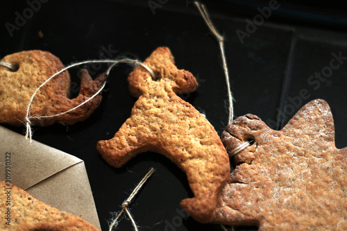 Merry Christmas. Gingerbread cookies and a stylish rustic Christmas gift in kraft packaging on a black background. Eco-friendly Christmas decorations with twine. Handwork with children. Hand made gift